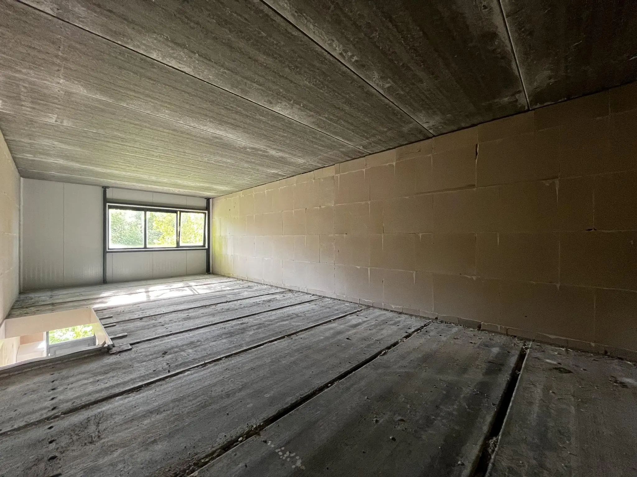 Lege betonnen ruimte in ruwbouwstaat met groot raam aan de achterzijde op Broekdijk West 19-4.